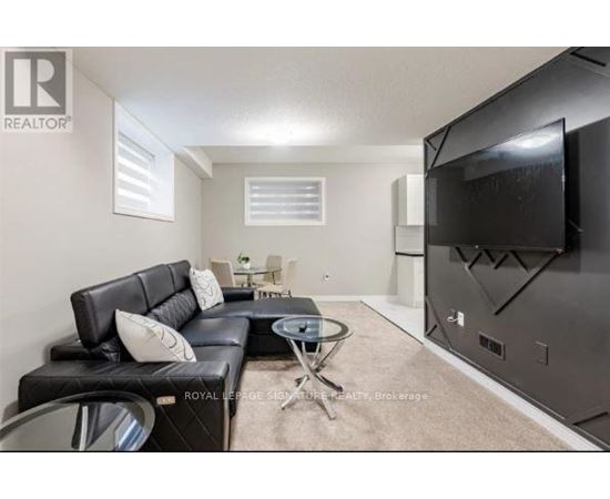 A living room with a black leather couch and a flat screen TV mounted on the wall.