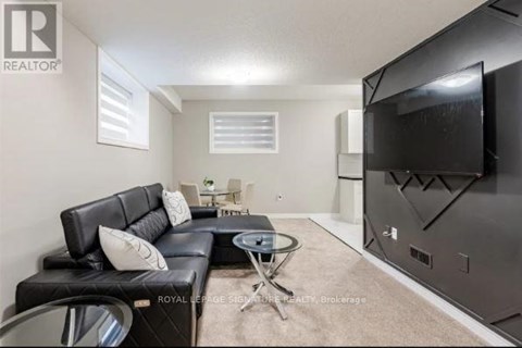 A living room with a black leather couch and a flat screen TV mounted on the wall.