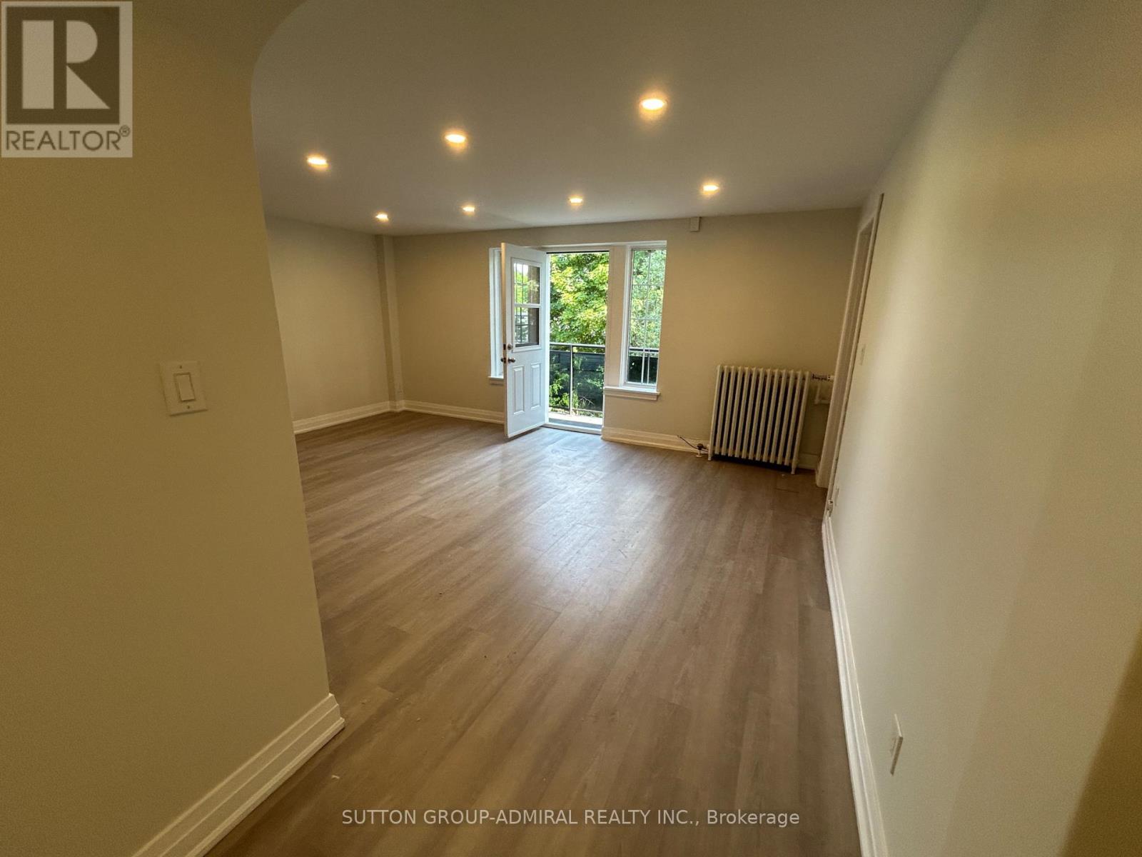A spacious room with wooden flooring and a sliding glass door leading to a balcony.