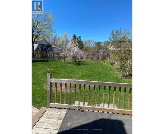 A wooden deck with a railing overlooks a green lawn and trees.