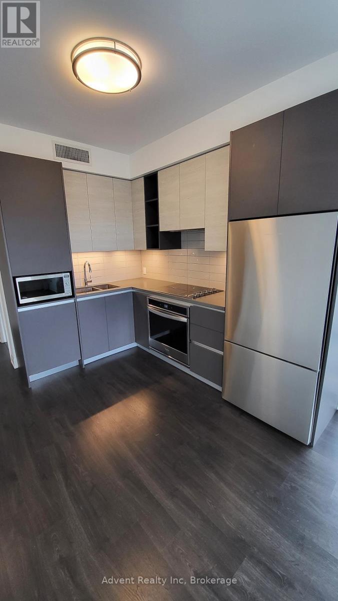 A modern kitchen with dark wood floors and stainless steel appliances.