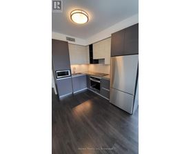 A modern kitchen with dark wood floors and stainless steel appliances.