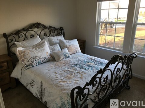 A bed with a white and blue comforter and matching pillows sits in a room with a window.