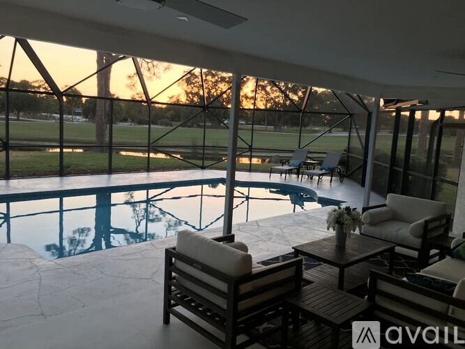 A patio with a table and chairs overlooking a pool and trees.