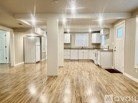 A spacious kitchen with wooden floors and white appliances.