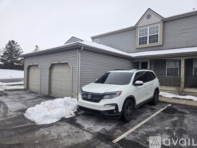 A white SUV is parked in front of a grey house with snow on the ground.