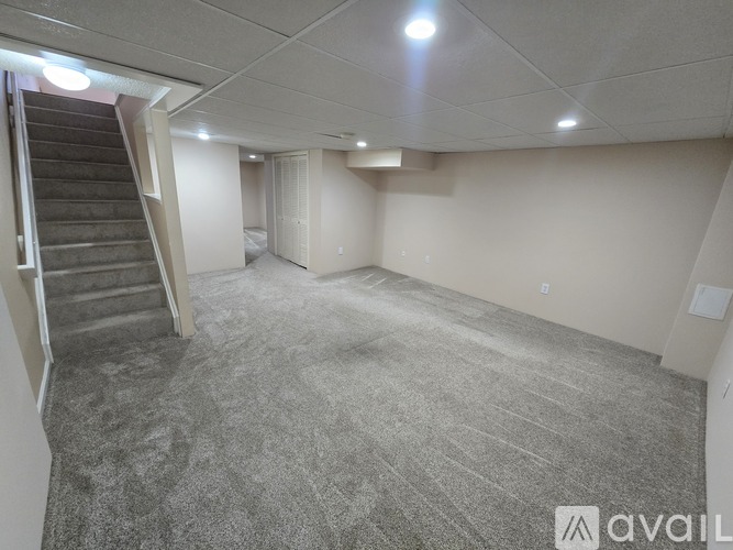 A spacious room with a carpeted floor and a staircase on the left side.