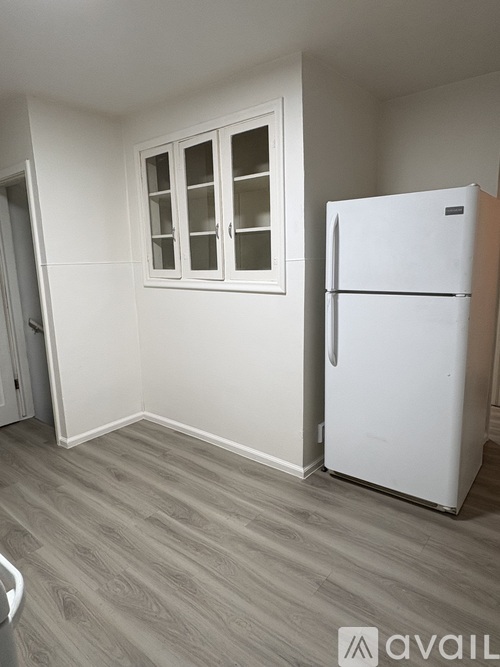 A white refrigerator is in a kitchen with wood flooring and white walls.
