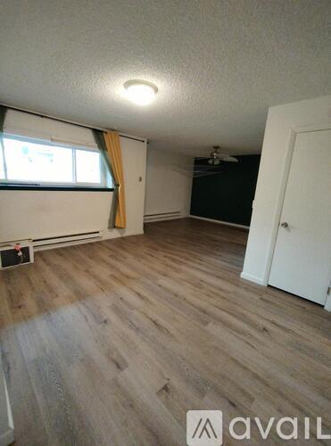 A room with wooden flooring and a window with yellow curtains.