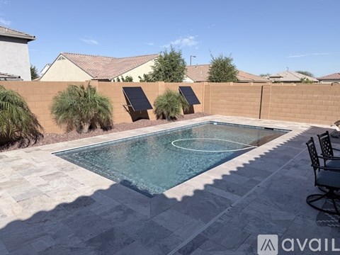 A pool with a tiled edge and a patio chair with a sun lounger in the background.