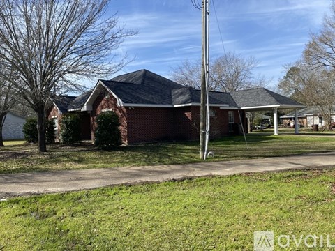 A house with a brick facade and a black roof is surrounded by a grassy lawn and leafless trees.