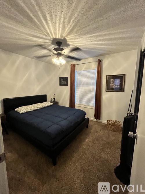 A bedroom with a bed, ceiling fan, and a window with blinds.