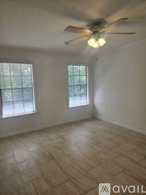 A room with a ceiling fan and two windows.
