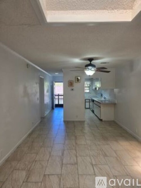 A room with a ceiling fan and light fixture, and a kitchen area with a sink and stove.