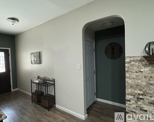 A room with a doorway leading to another room, a shelf with glasses on it, and a picture on the wall.
