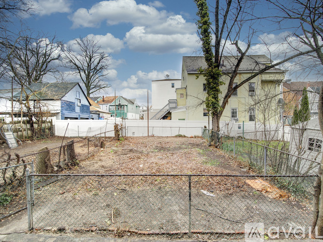 A fenced area with a dirt ground and trees in front of a row of houses.