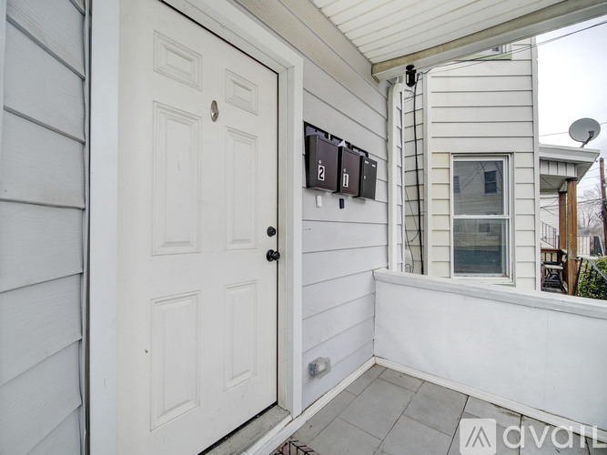 A white door is open to a small balcony with a wall-mounted thermostat.
