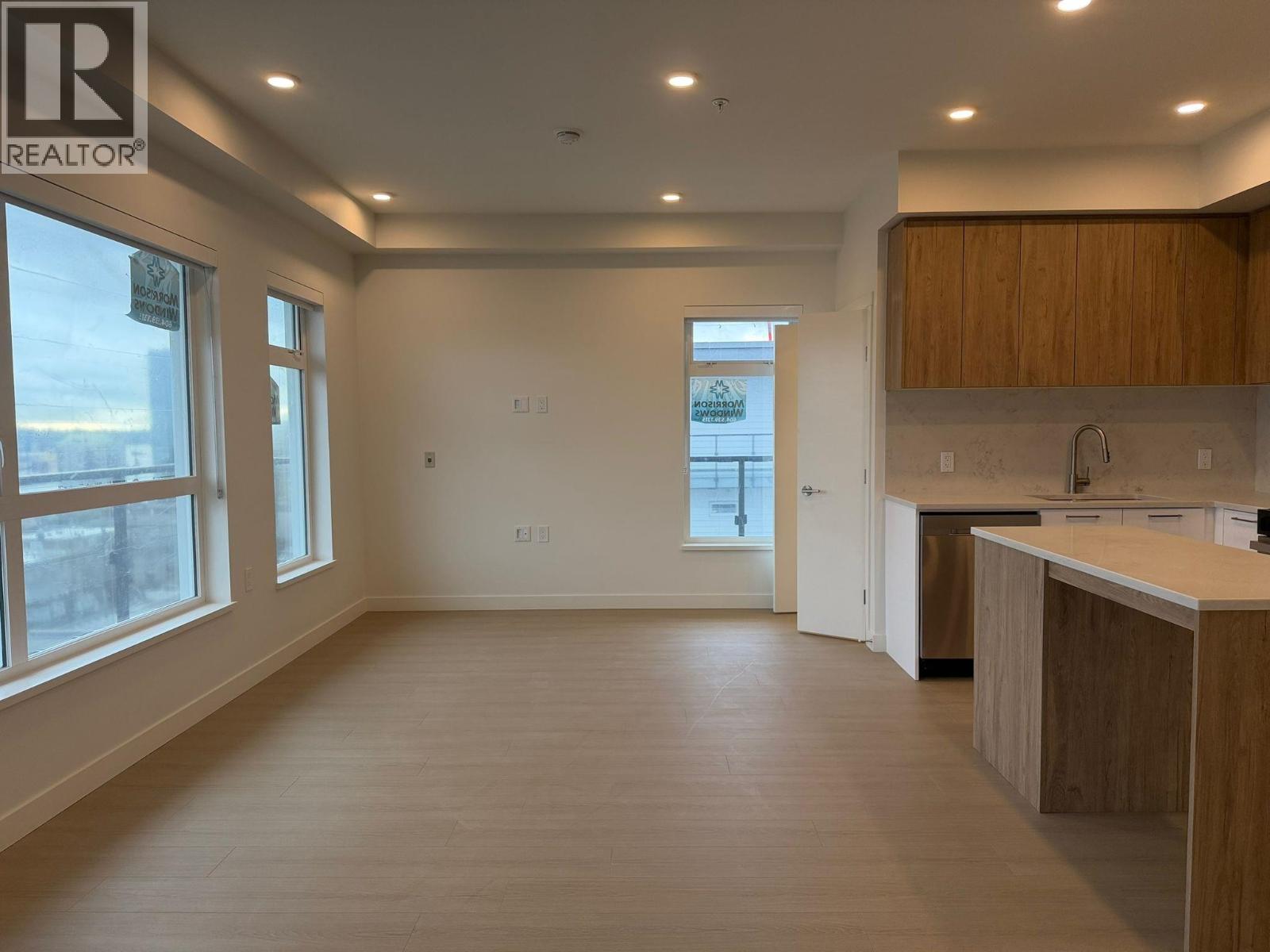 A spacious room with wooden floors and a kitchen area with white cabinets.