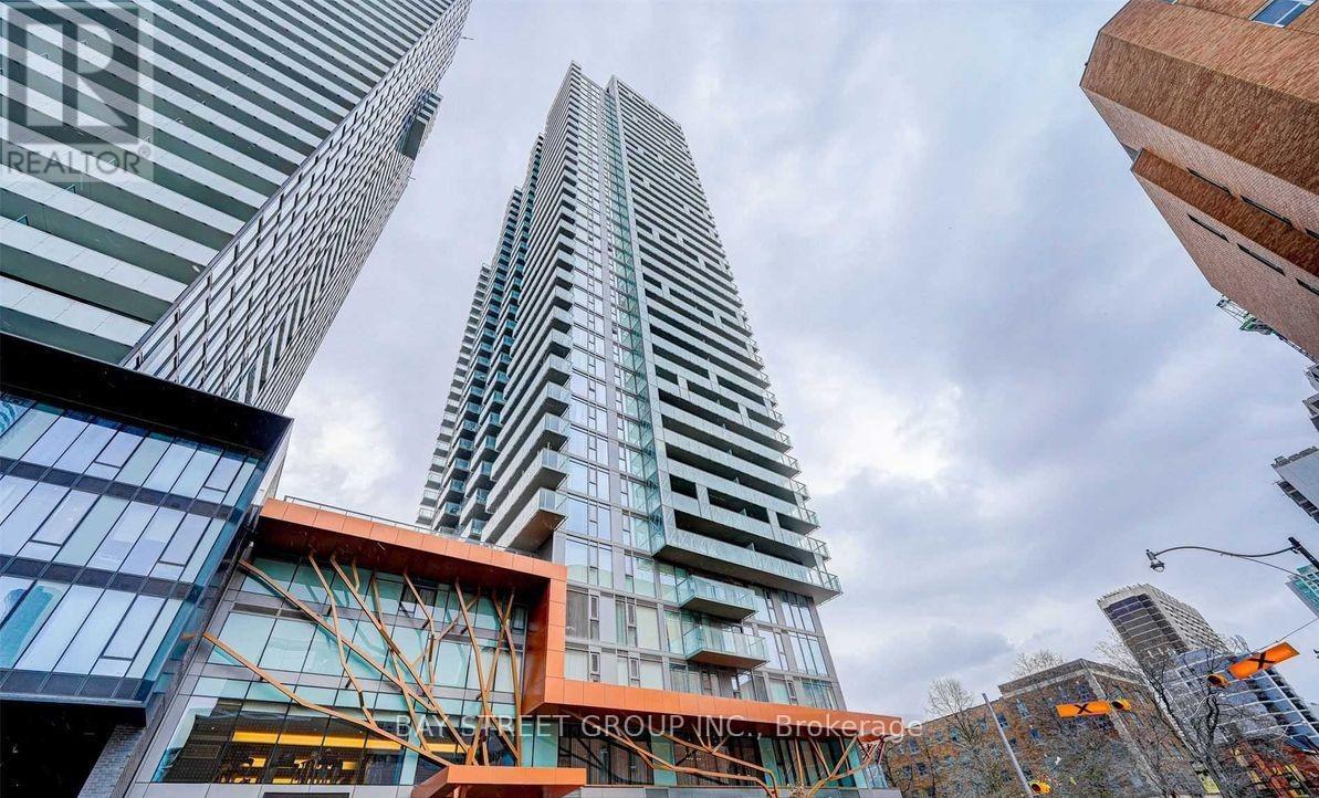 A tall building with a glass facade stands in front of other buildings.