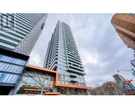 A tall building with a glass facade stands in front of other buildings.