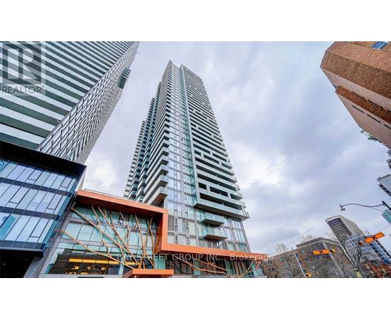 A tall building with a glass facade stands in front of other buildings.