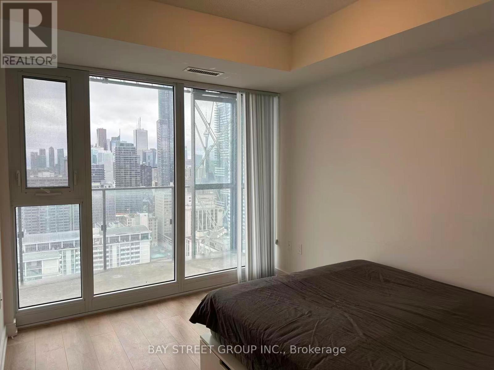 A bedroom with a large bed and a view of the city through the windows.