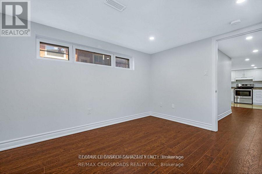 A room with white walls and wooden flooring, with a kitchen visible in the background.