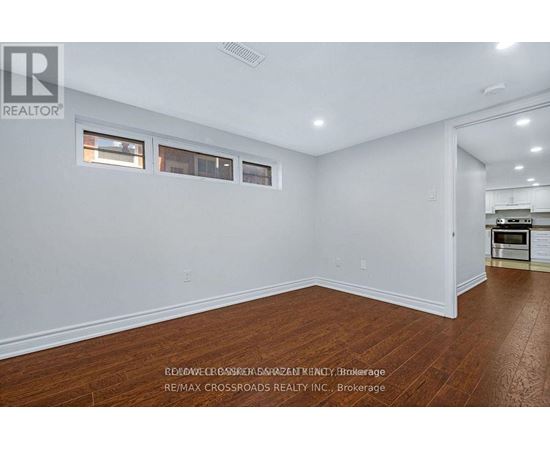 A room with white walls and wooden flooring, with a kitchen visible in the background.