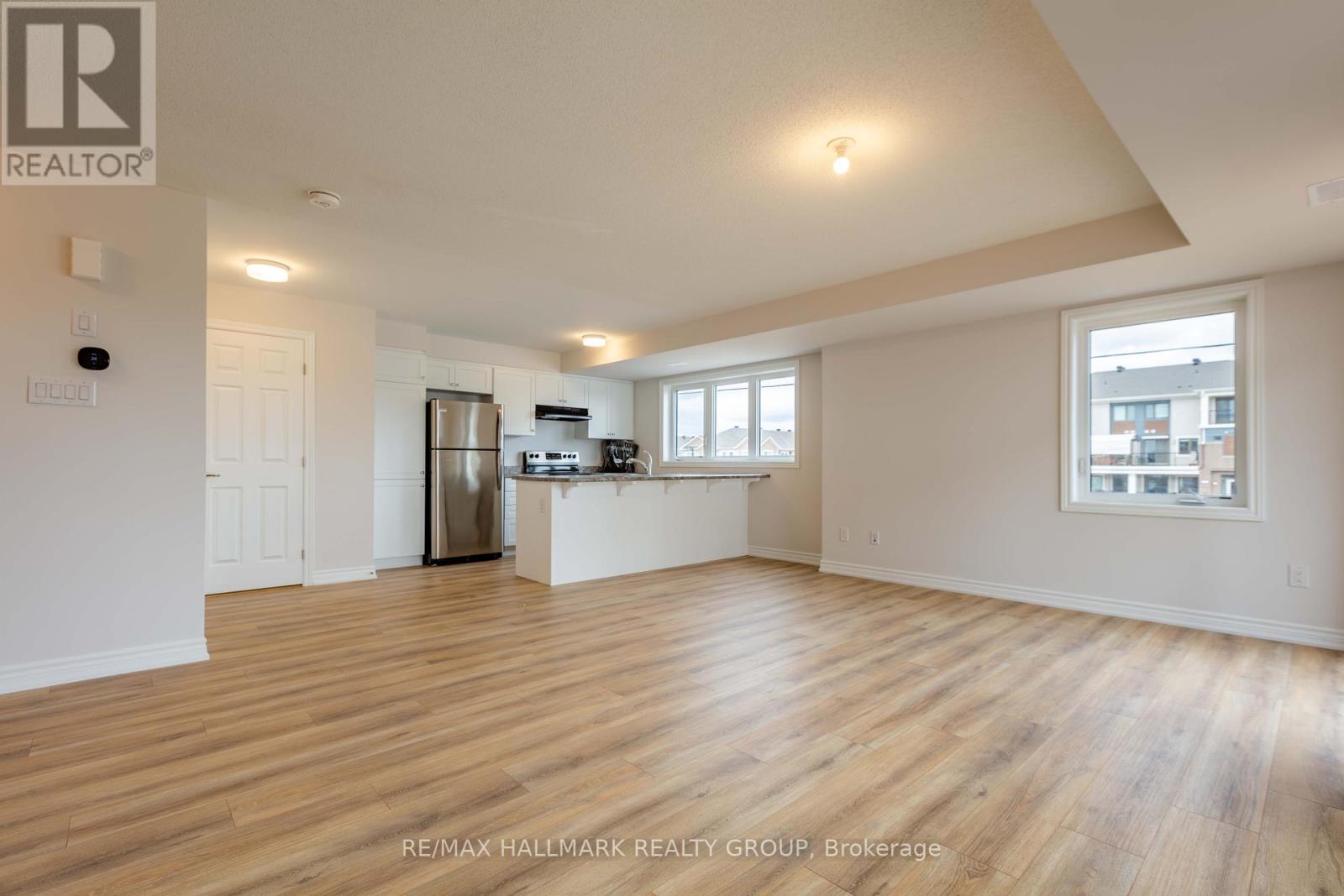 A spacious room with wooden flooring and a kitchen area in the background.
