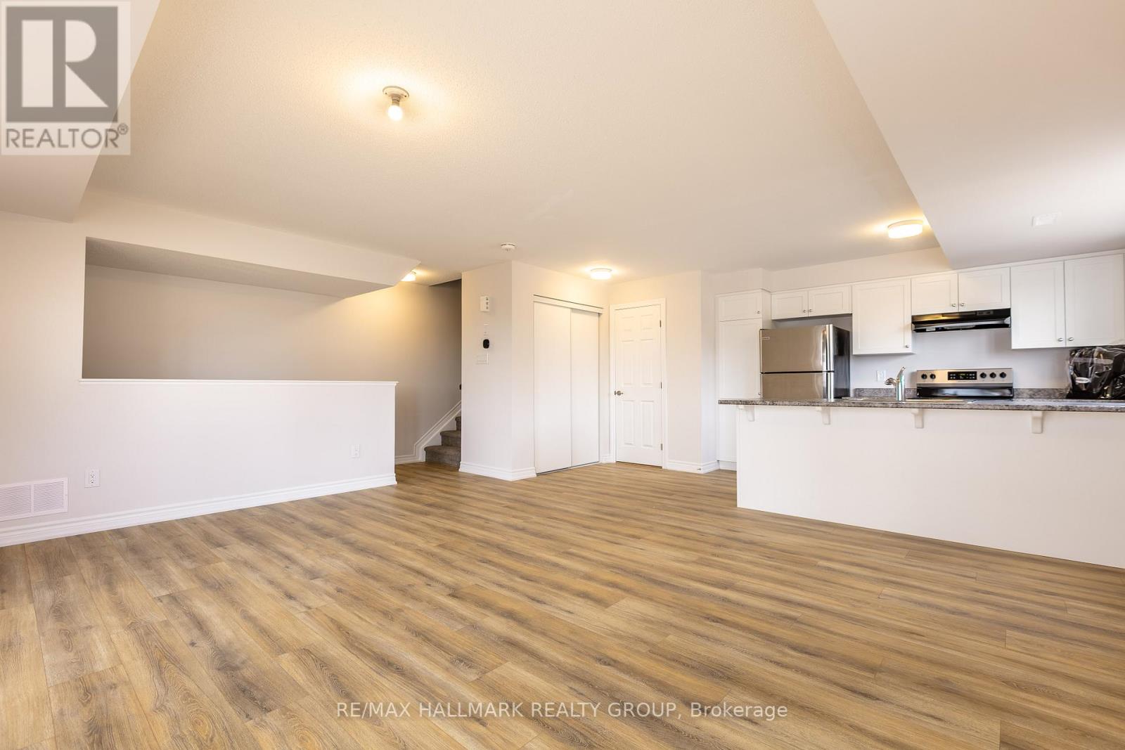 A spacious room with wooden flooring and white walls, featuring a kitchen area with stainless steel appliances.
