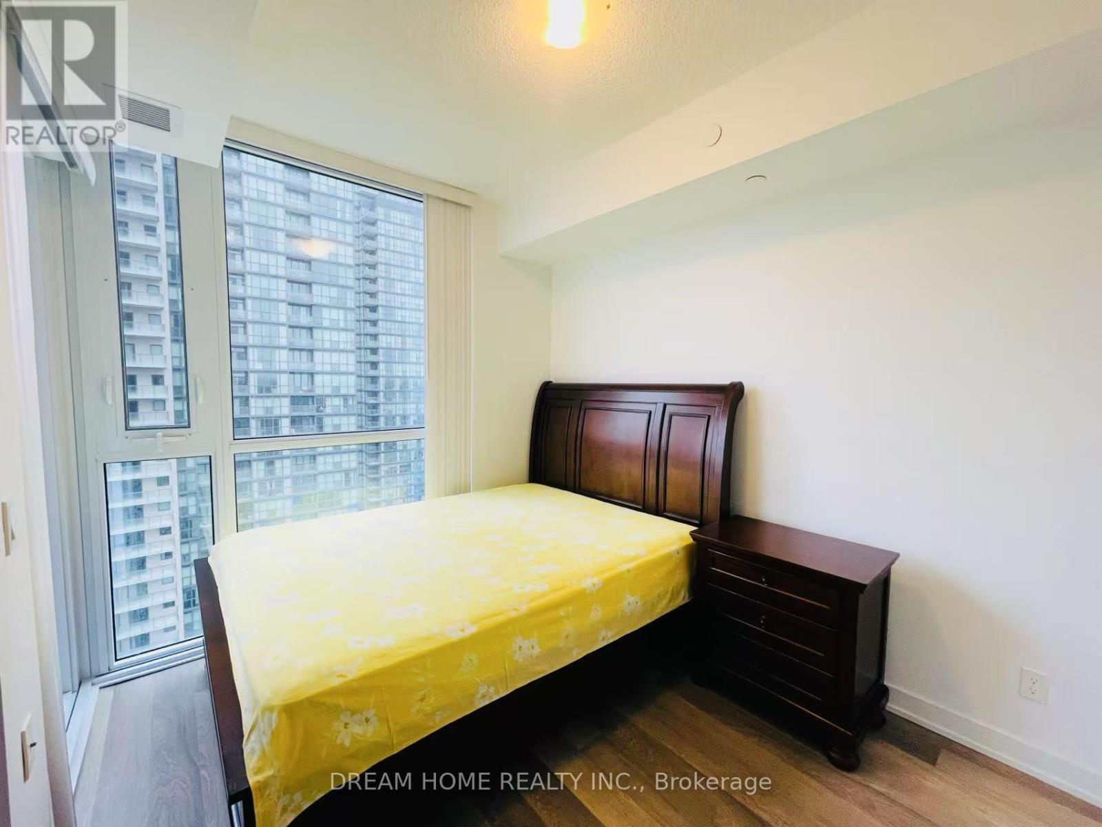 A bedroom with a bed, nightstand, and window with a view of a building.