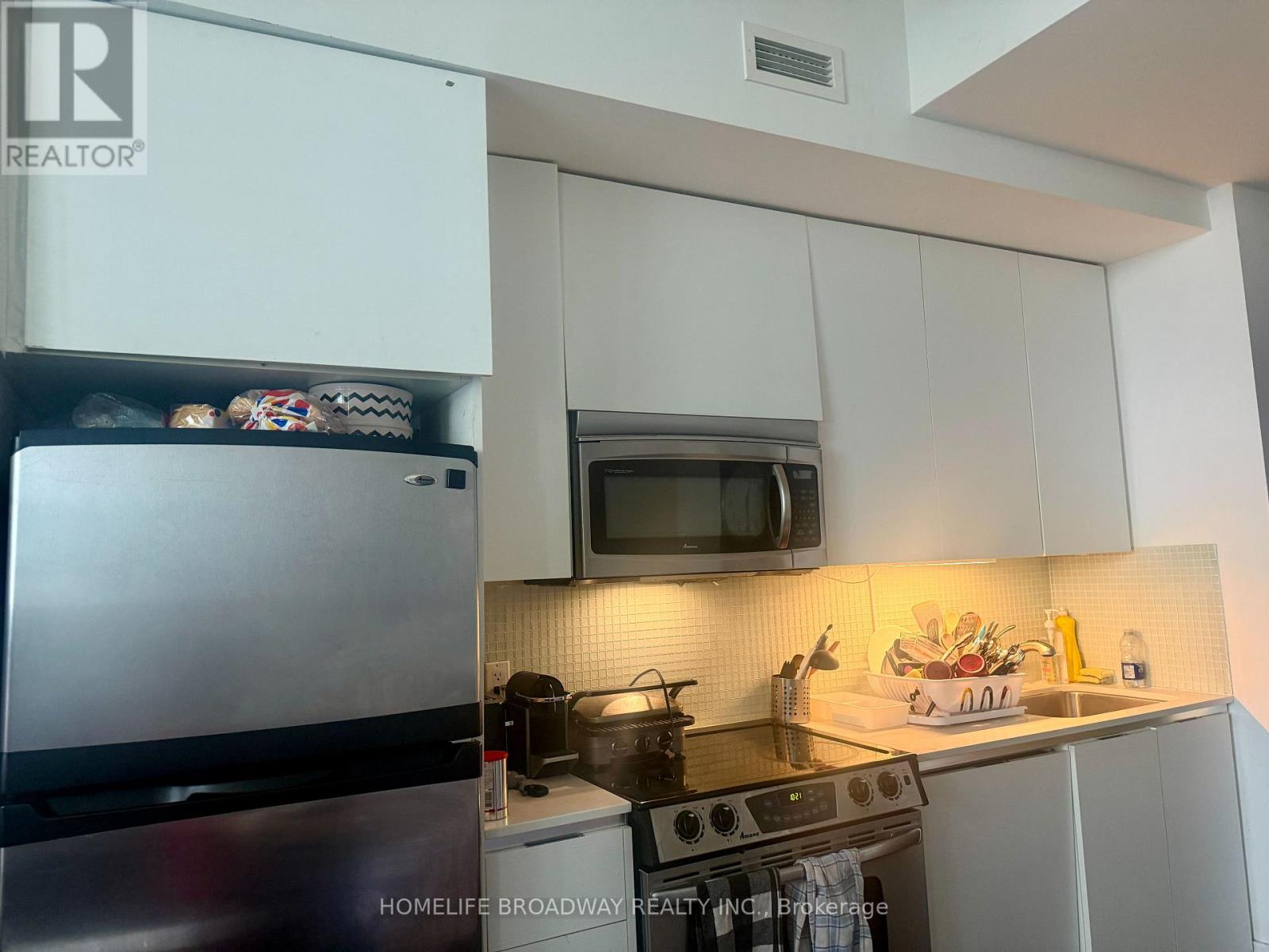A kitchen with white cabinets and a stainless steel refrigerator.