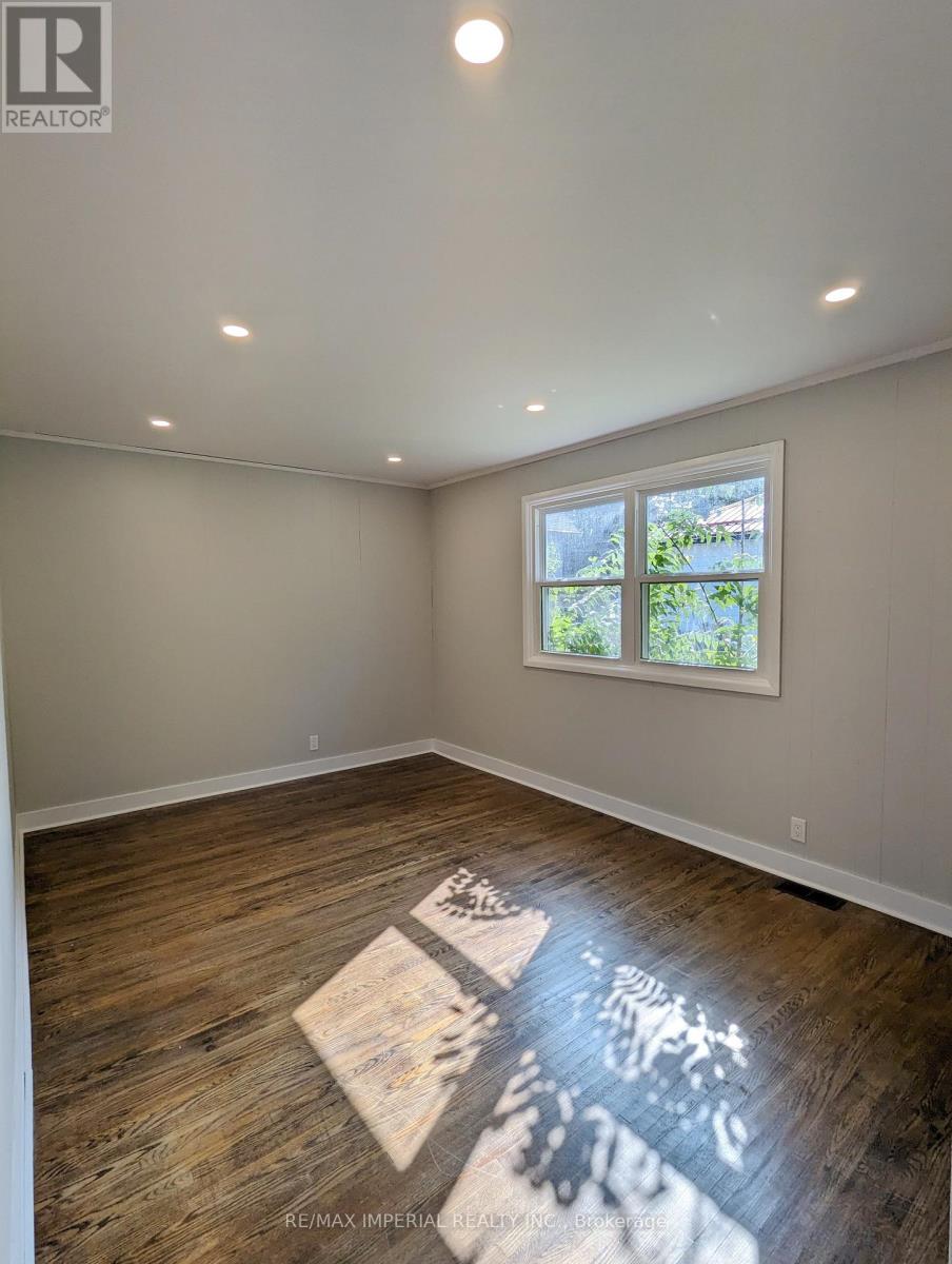 A room with wooden flooring and a window showing greenery outside.