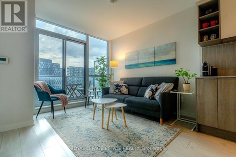 A living room with a black couch, a blue chair, and a table with a plant on it.