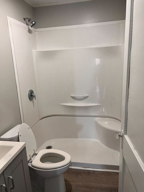 A white toilet is in a small bathroom with a walk-in shower.