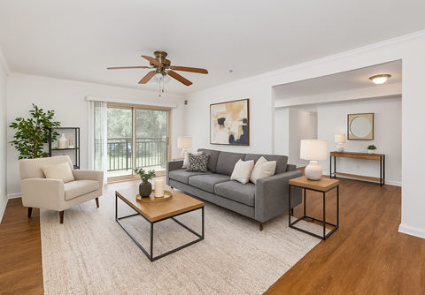 A living room with a grey couch, a white chair, a wooden coffee table, and a ceiling fan.