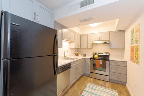 A black refrigerator stands in a kitchen with white cabinets and a stove.