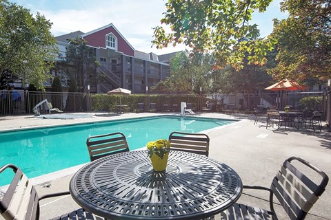 A round table with a vase of flowers on it sits in front of a pool.