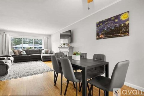 A living room with a grey sofa, a black dining table with grey chairs, and a painting on the wall.