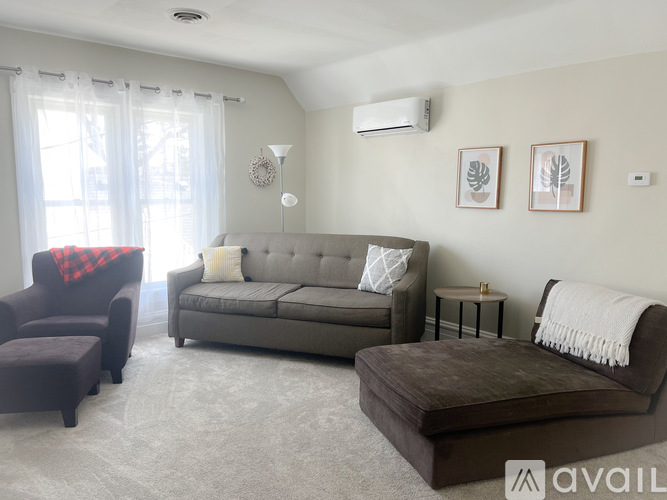 A living room with a grey couch, a brown ottoman, and a red blanket on a chair.