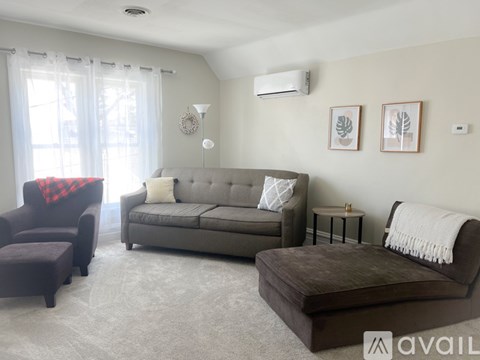 A living room with a grey couch, a brown ottoman, and a red blanket on a chair.