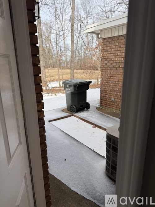 A black trash can is on a snowy sidewalk.