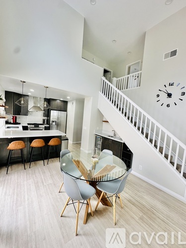 A modern kitchen with a dining table and chairs in the foreground and a staircase in the background.