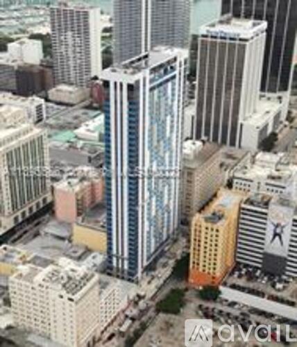 A tall building with a blue glass facade stands out among other buildings in a cityscape.