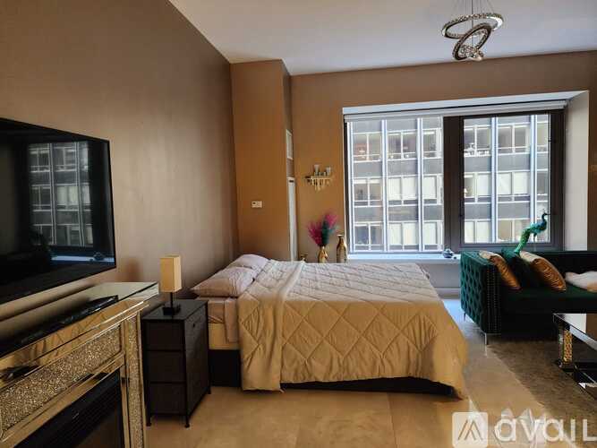 A bedroom with a large bed, a television, and a window overlooking a building.