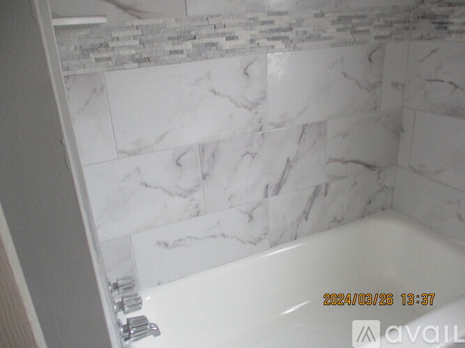 A white bathtub with a marble wall behind it.