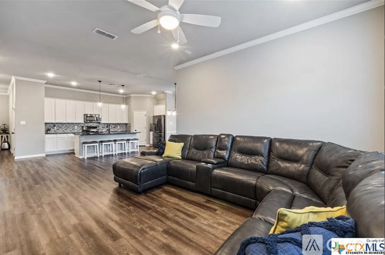 A living room with a black leather couch and a ceiling fan.
