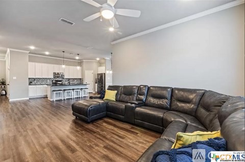 A living room with a black leather couch and a ceiling fan.