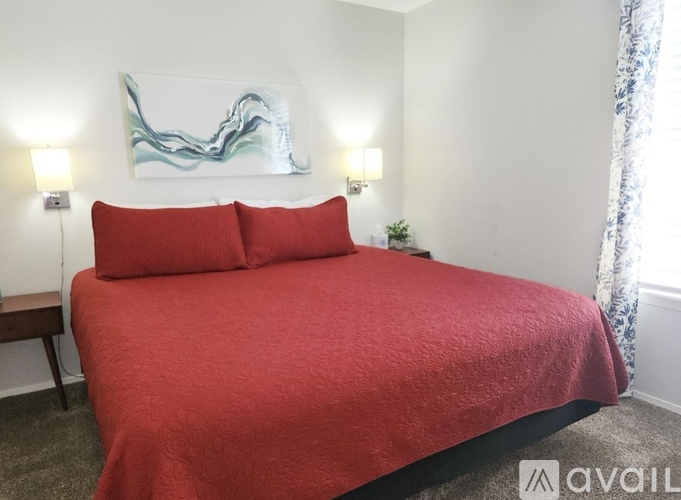 A bed with a red cover and two red pillows in a room with a white wall and a painting.