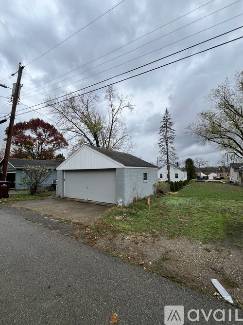 A white garage is situated on a grassy area next to a road.